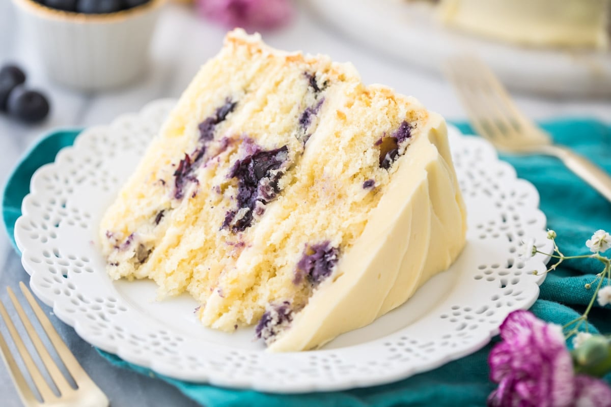 slice of cake consisting of three layers of lemon cake studded with blueberries layered with a homemade lemon icing