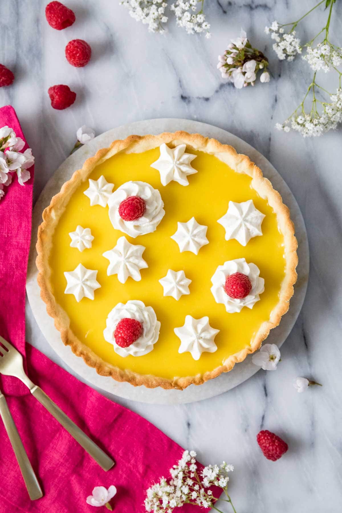 Overhead view of a lemon tart decorated with piped whipped cream and raspberries.