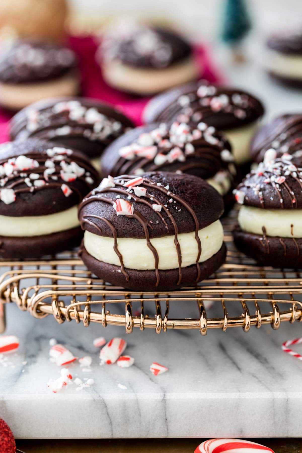 peppermint bark whoopie pies drizzled with chocolate and topped with crushed candy canes on gold metal cooling rack