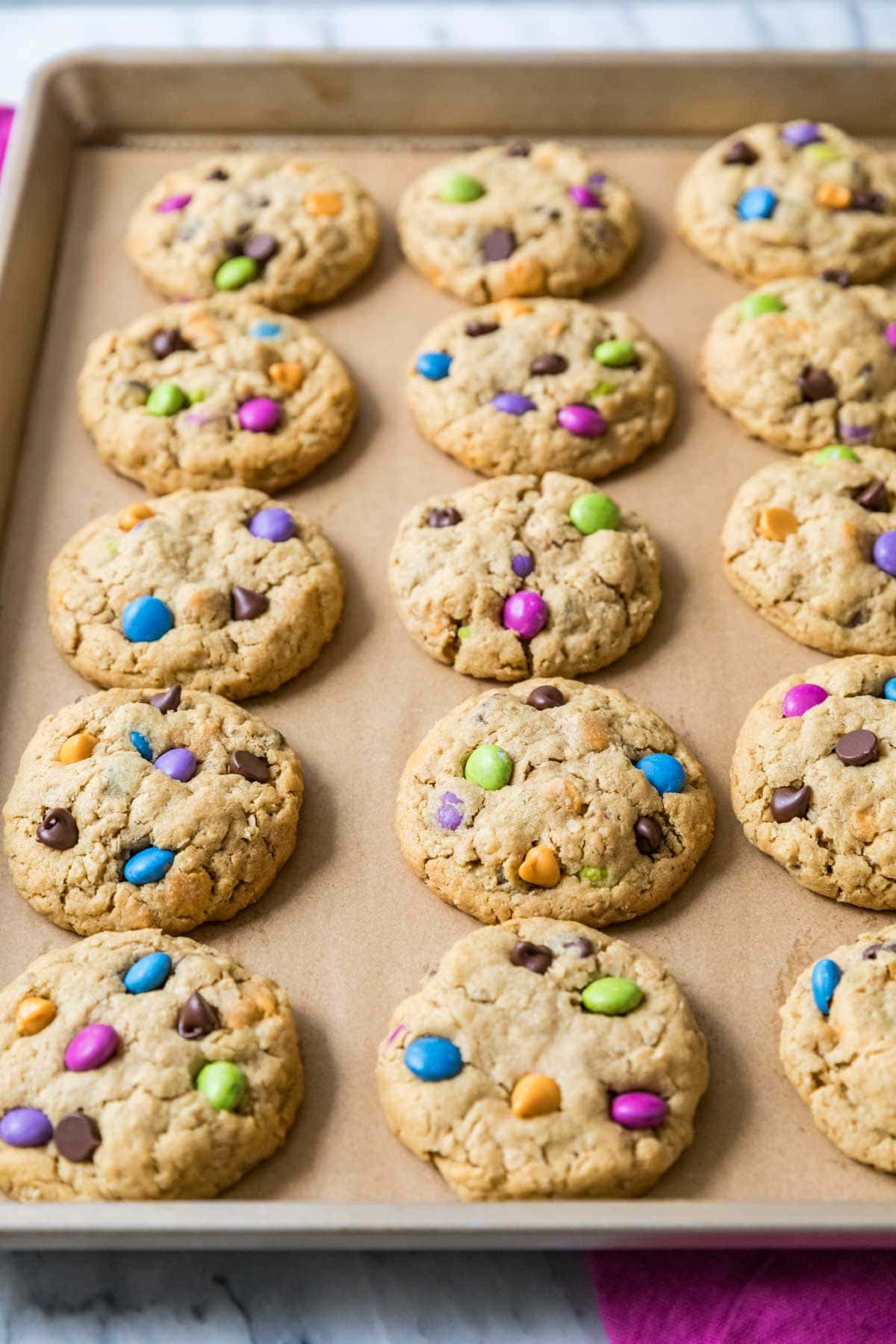 Rows of monster cookies made with colorful candies on a baking sheet.