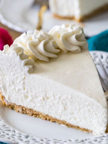 slice of no-bake cheesecake topped with whipped cream on a white decorative plate