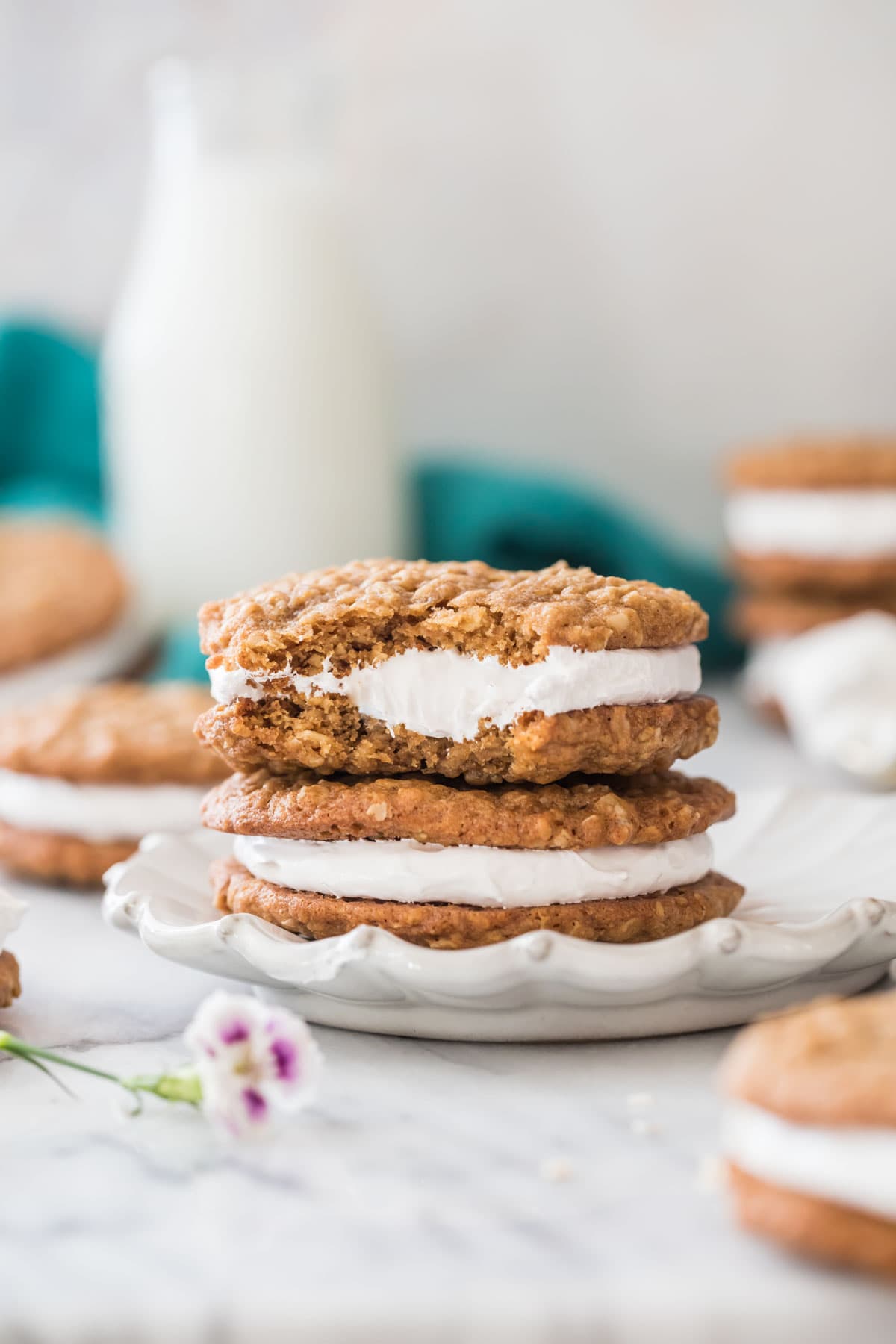 two oatmeal cream pies stacked on top of each other on a white decorative plate, with the top cream pie missing a bite
