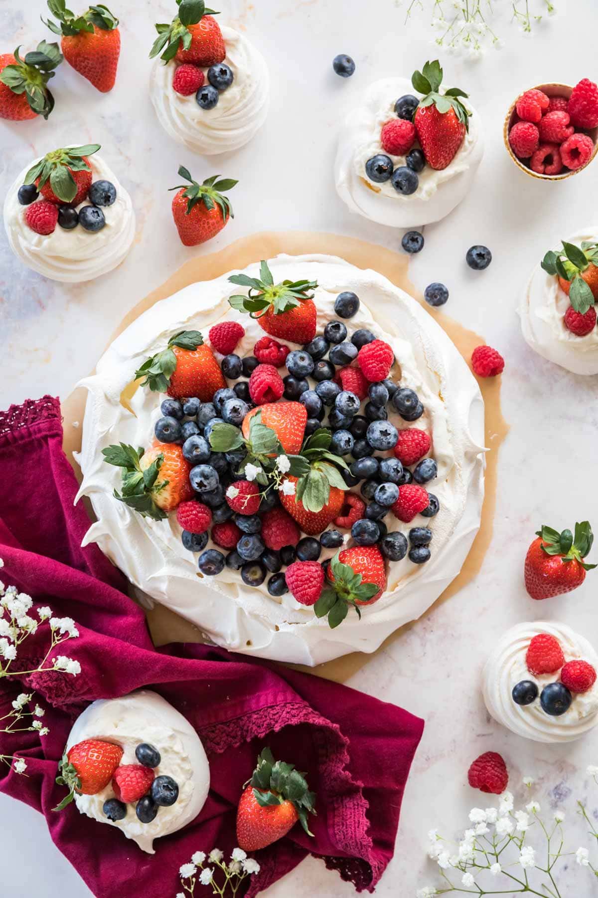 Large pavlova topped with fruit and whipped cream surrounded by mini pavlovas.