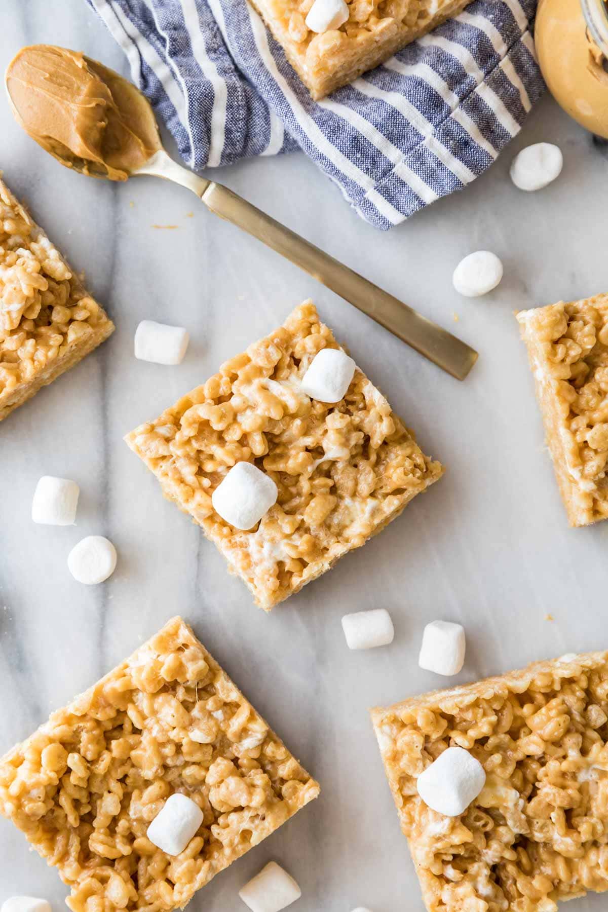 Rice krispie treats scattered across a marble surface with mini marshmallows throughout.
