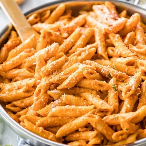 Wooden spoon resting in a large skillet of penne alla vodka topped with parmesan cheese.