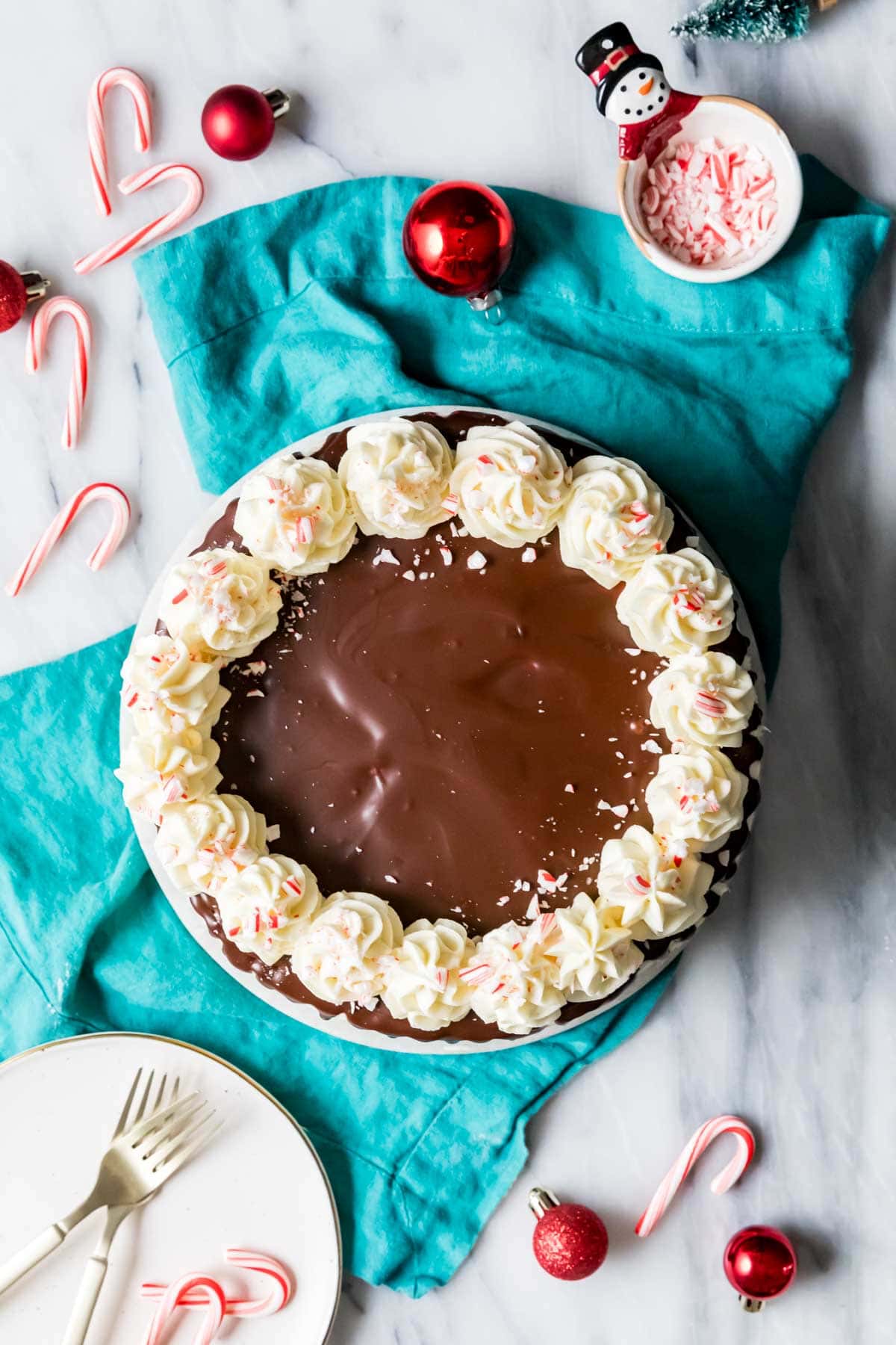 Overhead view of a cake topped with chocolate ganache, piped frosting swirls, and crushed peppermint candies.