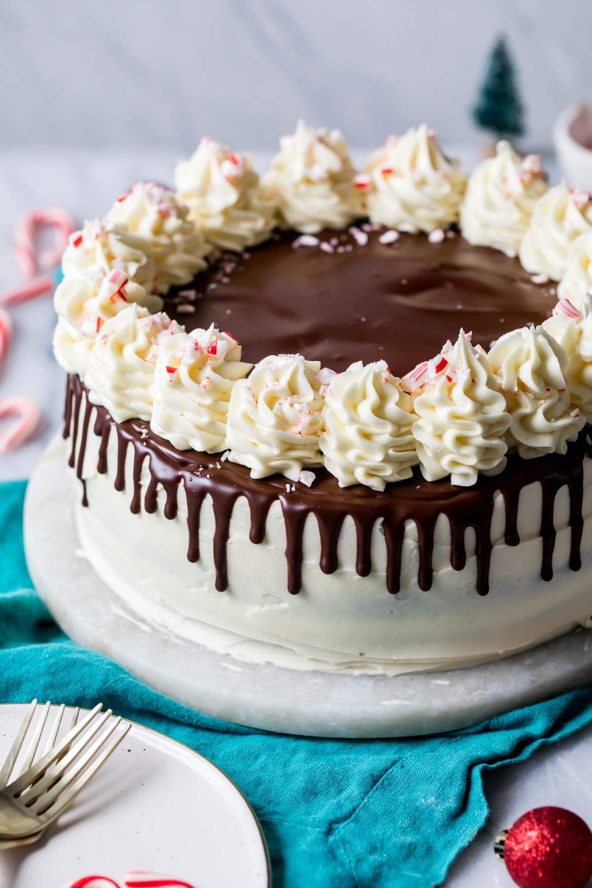 Peppermint bark cake decorated with chocolate ganache drip, white chocolate buttercream swirls, and crushed candy canes.