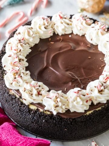 Overhead view of a peppermint bark cheesecake topped with chocolate ganache, whipped cream, and crushed peppermint candy.