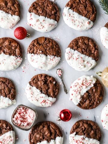 Overhead view of chocolate peppermint bark cookies that have been half dipped in white chocolate and sprinkled with crushed candy canes.