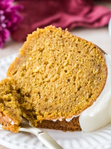 Slice of pumpkin bundt cake topped with cream cheese glaze on a plate with a fork taking one bite.