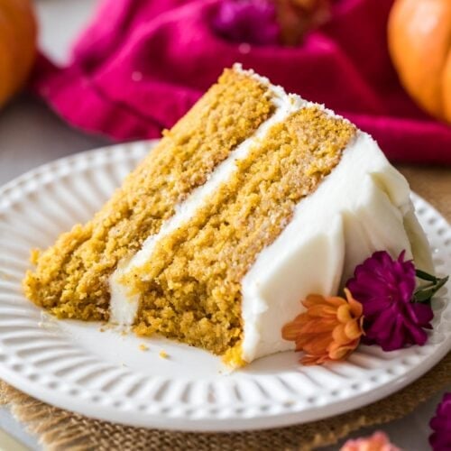 Slice of pumpkin cake frosted with cream cheese frosting on a white plate.