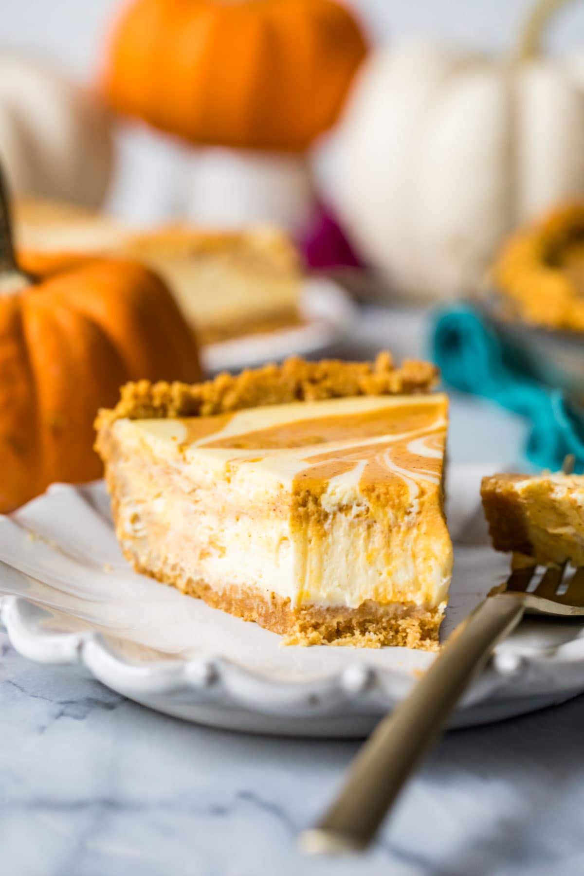 Slice of swirled pumpkin pie and cheesecake hybrid on a plate with one bite missing.