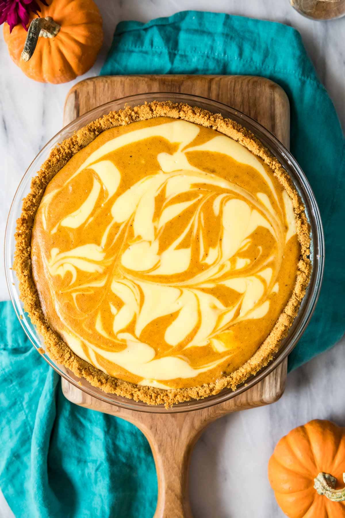 Overhead view of a swirled pumpkin cheesecake pie in a wood cutting board.