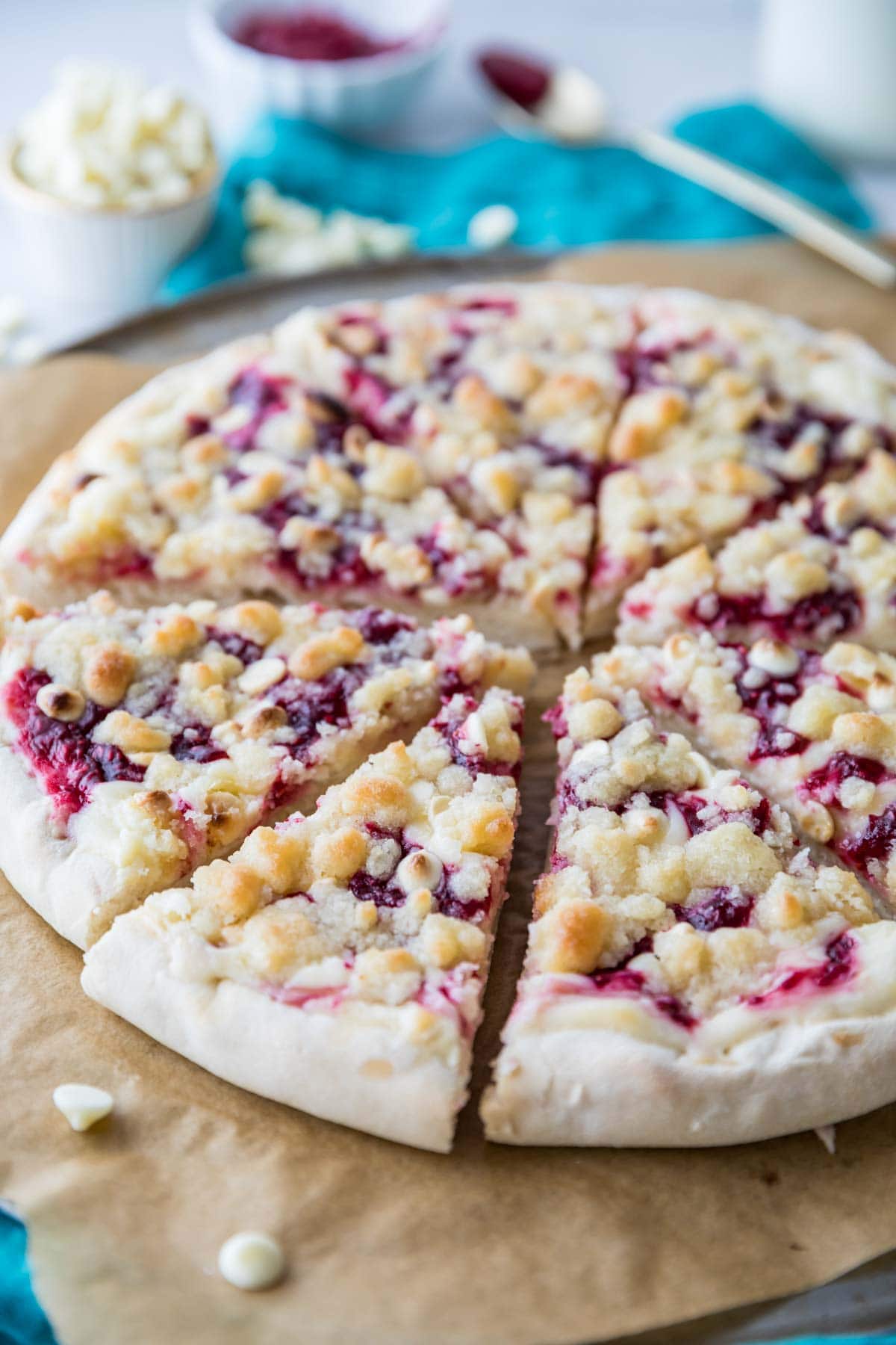 Close-up view of a raspberry cheesecake dessert pizza topped with white chocolate chips and streusel.