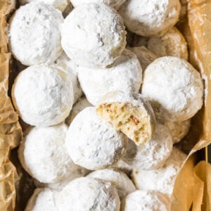 Overhead view of snowball cookies in a parchment lined bread pan with one cookie missing a bite.