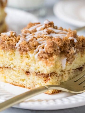 Slice of sour cream coffee cake with a fork on a white plate.