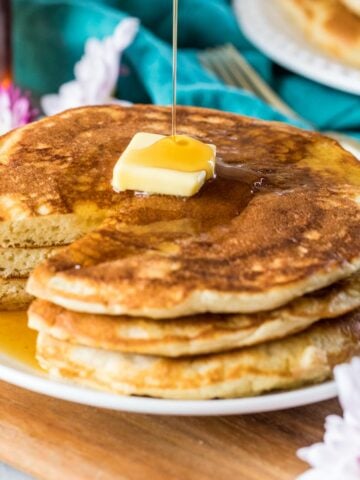 Syrup being poured over a buttered stack of sourdough pancakes.