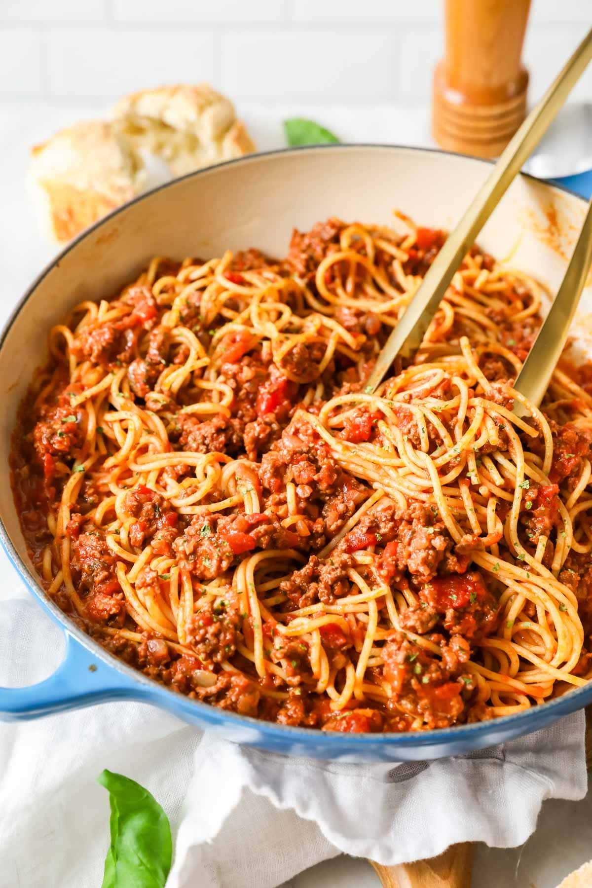 Tongs tossing spaghetti with meat sauce in a large pot.