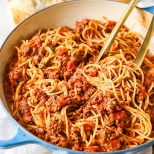 Tongs tossing spaghetti with meat sauce in a large pot.