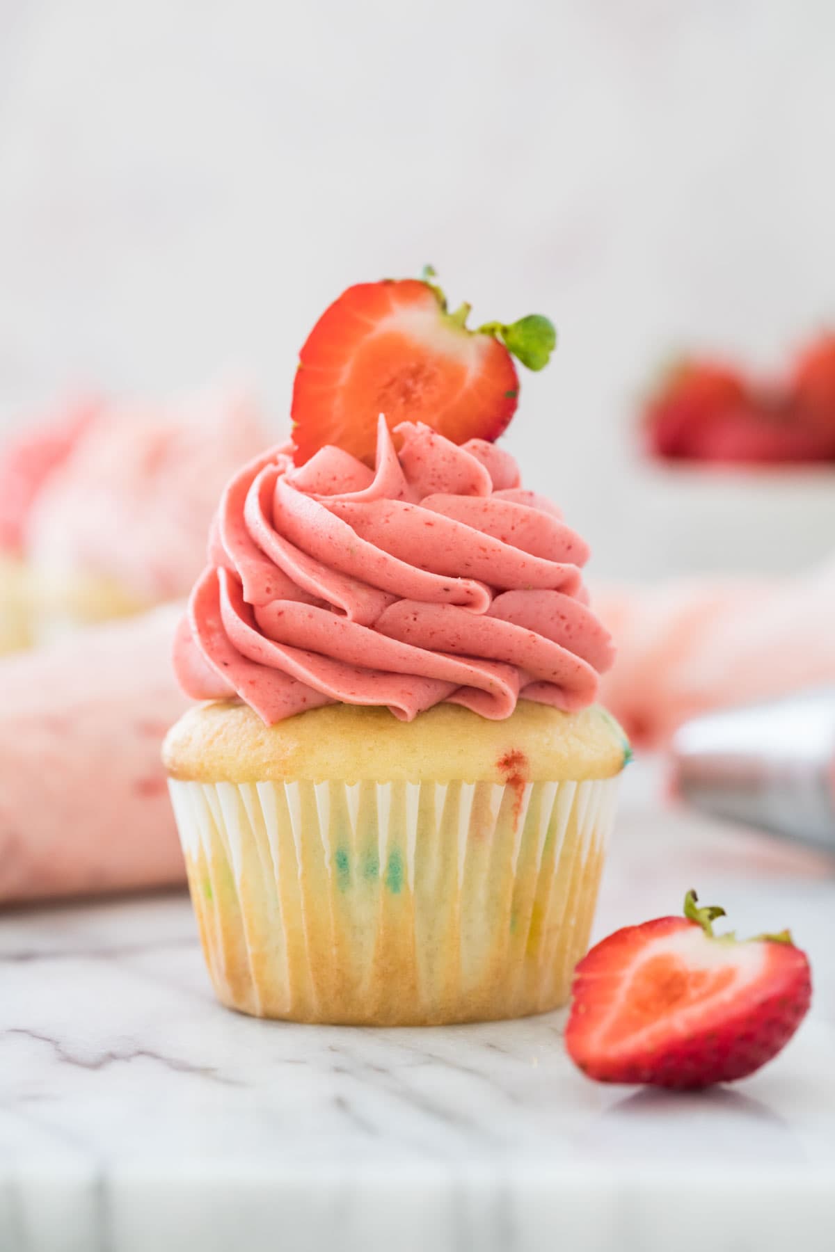 Vanilla cupcake topped with bright pink strawberry frosting and a halved fresh strawberry