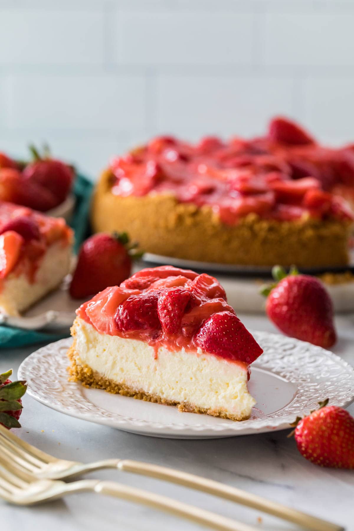 Slice of strawberry cheesecake on a plate with more cheesecake in the background.