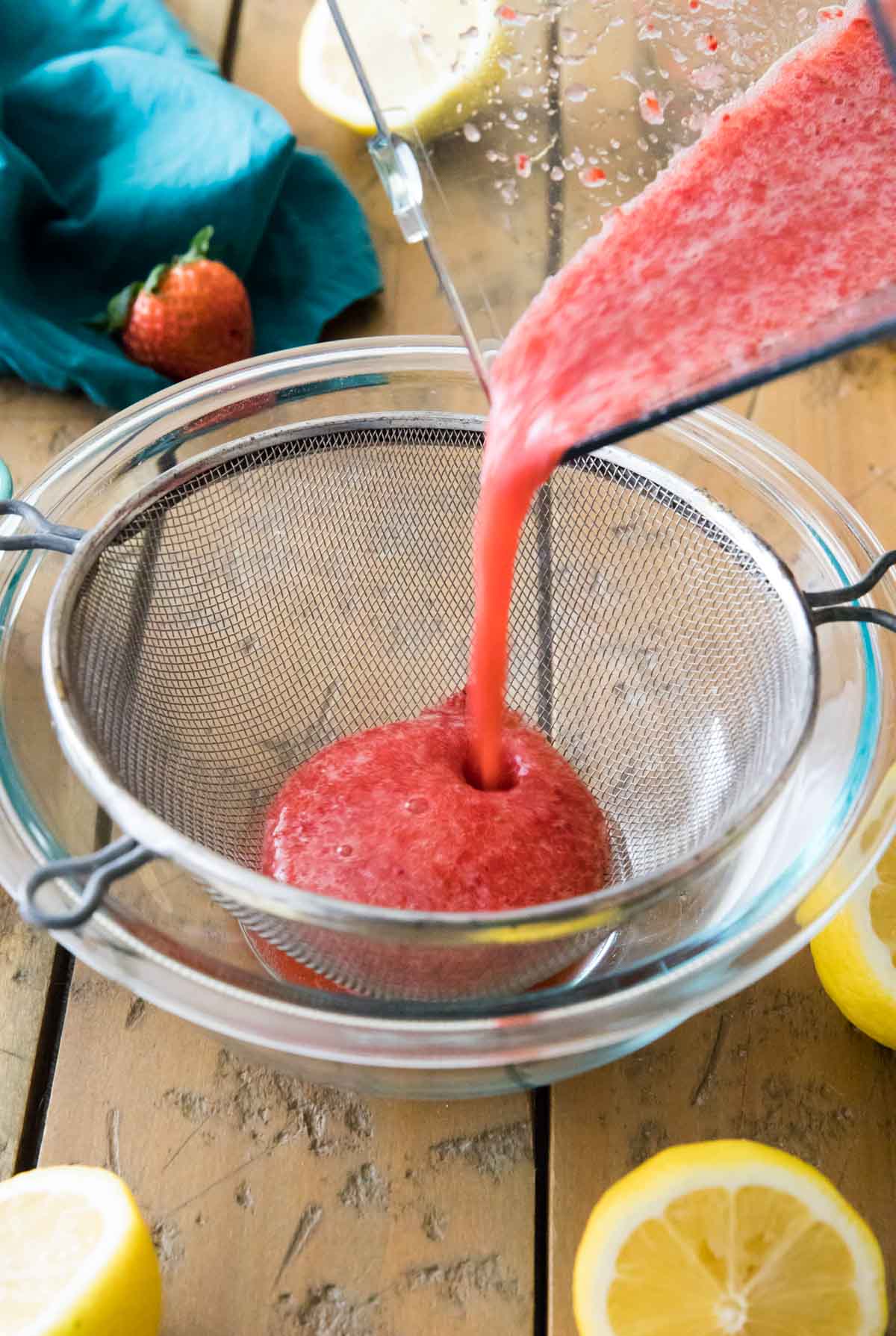 strawberry puree being poured through a fine mesh strainer into a bowl