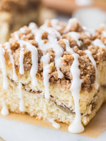 square slice of coffee cake with a cinnamon swirl middle, crumb topping, and vanilla drizzle glaze