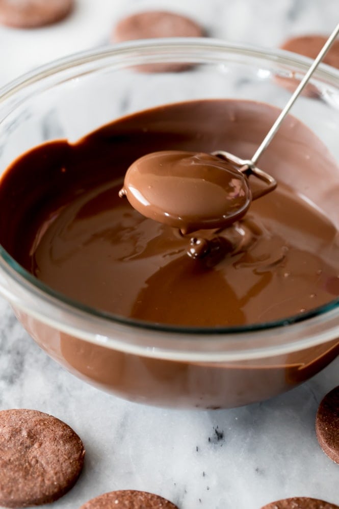 A chocolate cookie that's just been dipped in a bowl of melted chocolate and lifted out for the excess chocolate to drip off