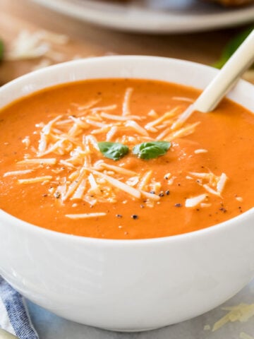 white bowl of hearty homemade tomato soup garnished with parmesan cheese, fresh basil, and cracked black pepper