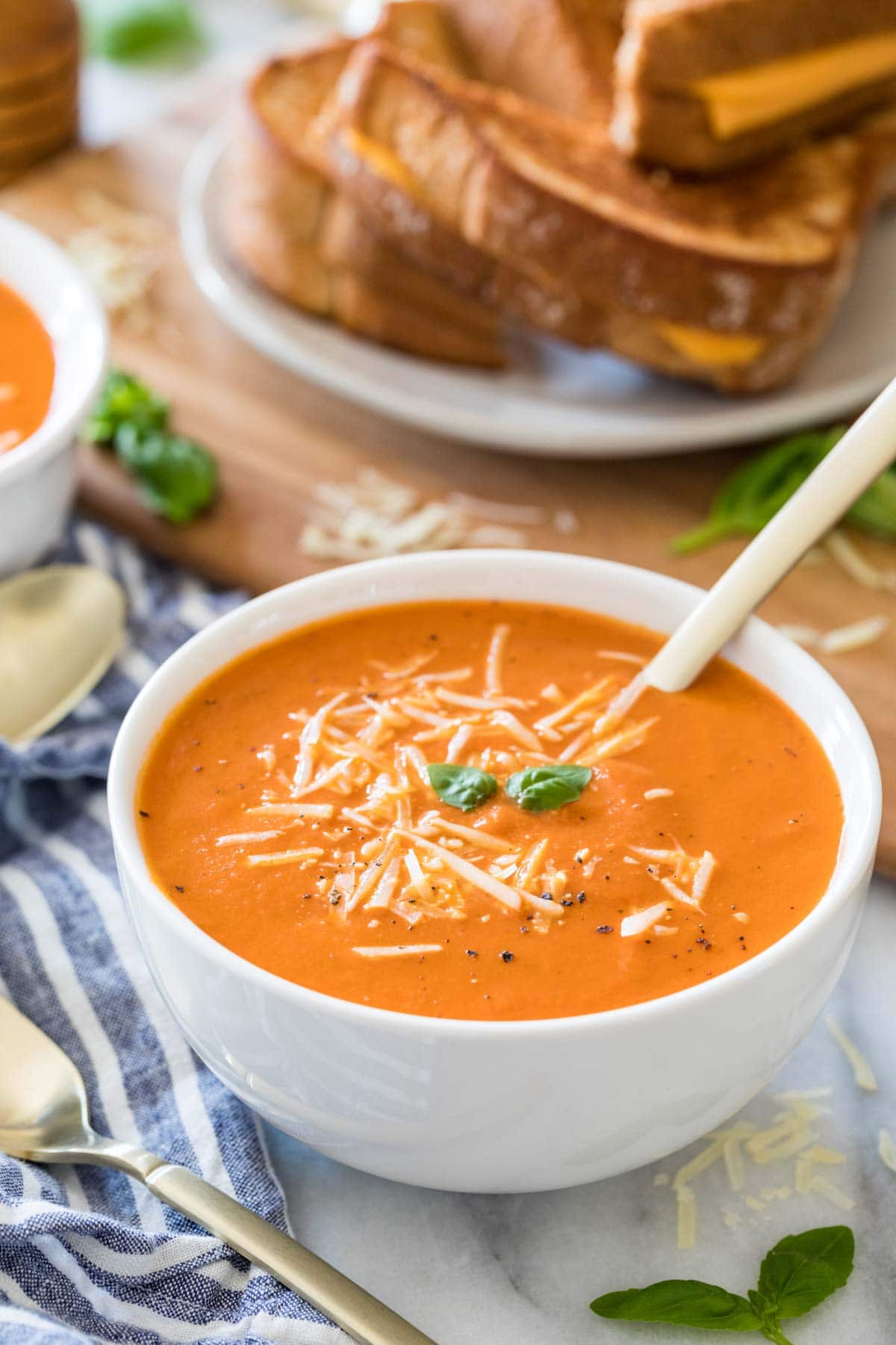 velvety tomato soup topped with cheese and fresh basil in white bowl with spoon dipped into it