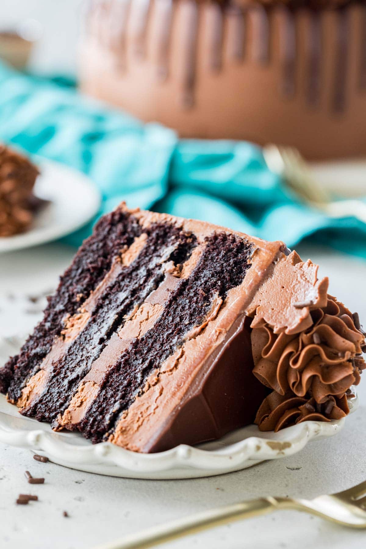 Slice of chocolate cake with chocolate ganache and chocolate frosting on a white plate.