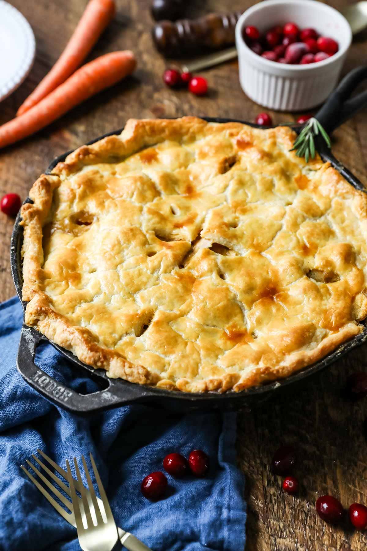 Pot pie made in a cast iron skillet with cranberries and carrots in the background.