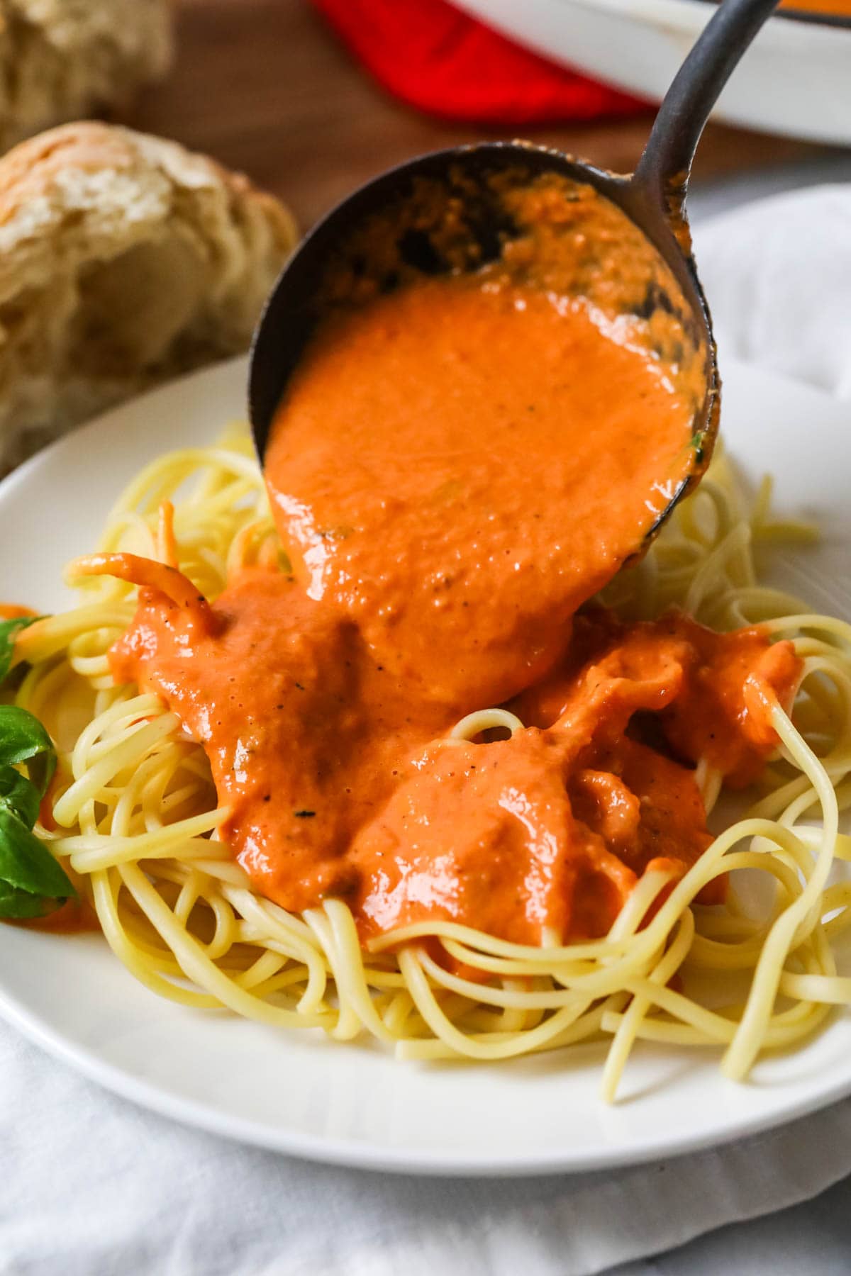 Ladle pouring homemade vodka sauce over spaghetti noodles.